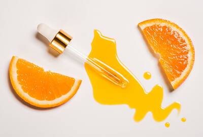 Contador de gotas com liquido laranja em uma mesa com fatias da fruta laranja representando a vitamina C que pode oxidar