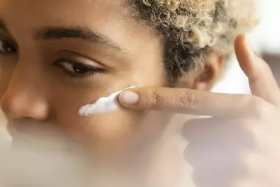 Jovem passando vitamina B3 no rosto, que ajudam a manter a pele saudavel, firme e hidratada.