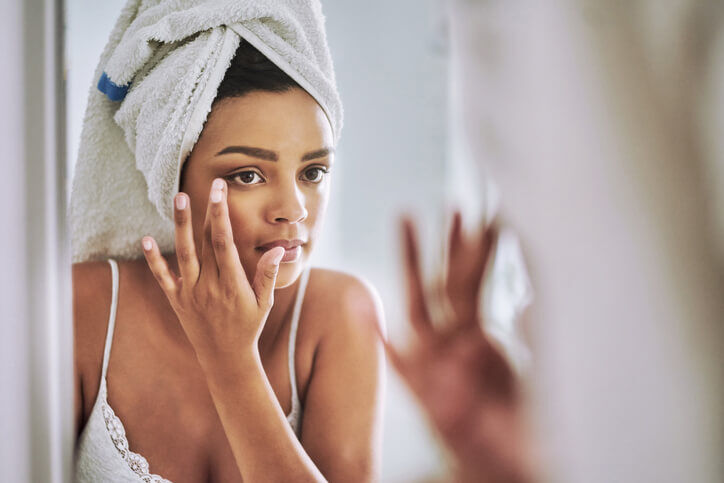 Mulher se olha no espelho ao passar creme anti-idade para rugas, bolsas e linhas de expressao ao redor dos olhos