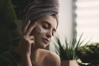 Mulher aplicando protetor solar no rosto e corpo, aprendendo a tecnica correta de aplicacao.
