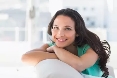 Mulher sorrindo com rosto encostado em suas maos