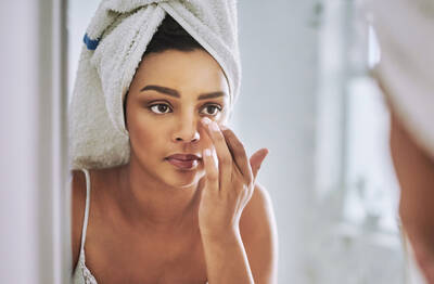 Mulher aplicando produto com cafeina na regiao dos olhos, conhecendo os beneficios para clarear olheiras e tratar rugas.