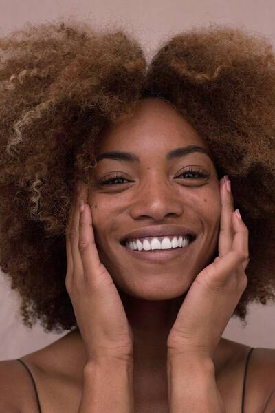 Mulher sorrindo, com as maos no rosto com pele oleosa mostrando brilho excessivo e espinhas