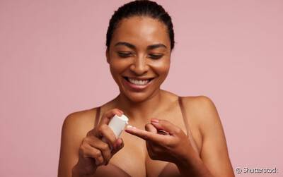 Mulher sorridente passando creme para prevenir e tratar sinais de envelhecimento da pele.