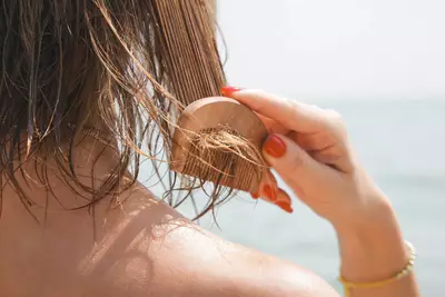 Mulher penteando seus fios na praia apos utilizar protetor solar para os cabelos