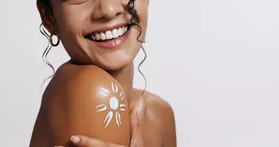 Mulher sorridente com protetor solar fluido no ombro