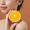 Foto de mulher segurando fatia de laranja proxima ao rosto simbolizando beneficios da vitamina C para a pele