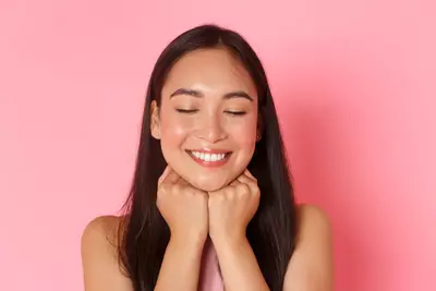 Mulher de cabelos escuros lisos sorrindo com o rosto com pele brilhante e hidratada como resultado do uso de cha de centella asiatica.