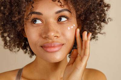 Mulher se questionando qual o melhor creme clareador de manchas no rosto enquanto aplica creme no rosto