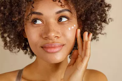 Mulher se questionando qual o melhor creme clareador de manchas no rosto enquanto aplica creme no rosto
