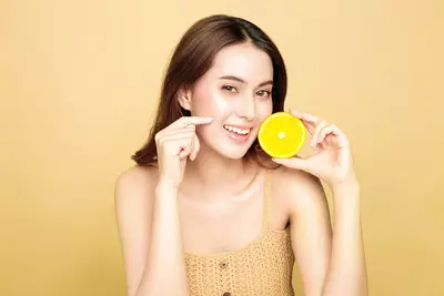 Mulher segurando uma laranja para representar o uso de vitamina c no rosto