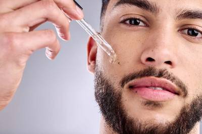 Homem com frasco de serum hidratante no rosto, um produto concentrado que oferece hidratacao intensa para a pele.