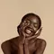 Mulher negra com cabelo preso em coque sorrindo enquanto aplica hidratante facial para pele oleosa com as maos.