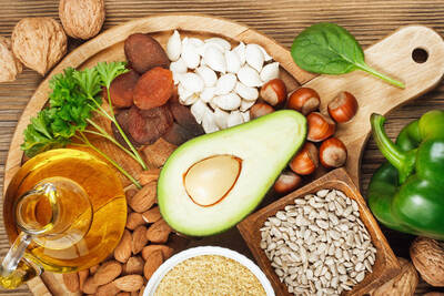 Foto de alimentos ricos em vitamina E, como abacate e castanhas, que podem ajudar a manter a pele saudavel.
