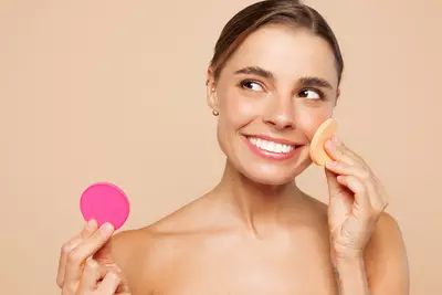 Mulher com maquiagem natural segurando esponja rosa em fundo bege