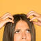 Mulher com falta de colageno capilar mexendo na raiz de seu cabelo com expressao de confusa.