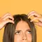 Mulher com falta de colageno capilar mexendo na raiz de seu cabelo com expressao de confusa.