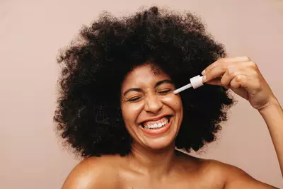 Mulher jovem sorrindo e passando serum antiacne no rosto