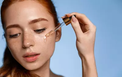 Menina ruiva passando serum de vitamina c na pele oleosa
