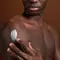 Homem negro sem camisa aplicando hidratante corporal com ceramidas no braco com as maos.
