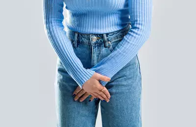 Mulher com as maos sob a virilha, pois sente coceira, um sintoma comum de alergias ou infeccoes na regiao intima.