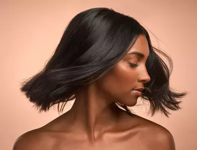 Mulher negra com cabelos lisos impecaveis apos fazer restauracao capilar