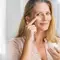 Mulher de 50 anos aplicando creme para a area dos olhos com o dedo indicador.