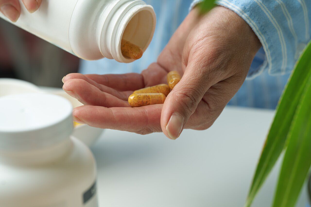Mao segurando capsulas de vitamina C que estao sendo colocadas a partir de um recipiente de remedios.