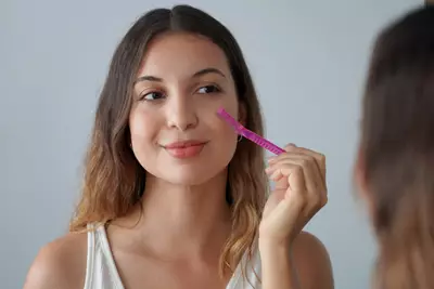 Jovem mulher realizando dermaplaning em seu rosto