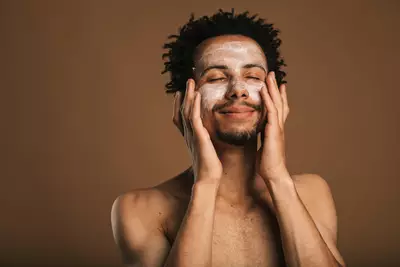 Homem jovem passando creme para pele seca no rosto