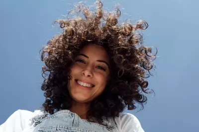 Jovem de cabelo cacheado olhando para a camera de uma posicao mais acima com seus cabelos caindo em volta de seu rosto, indicando o poder de produtos de crescimento capilar.