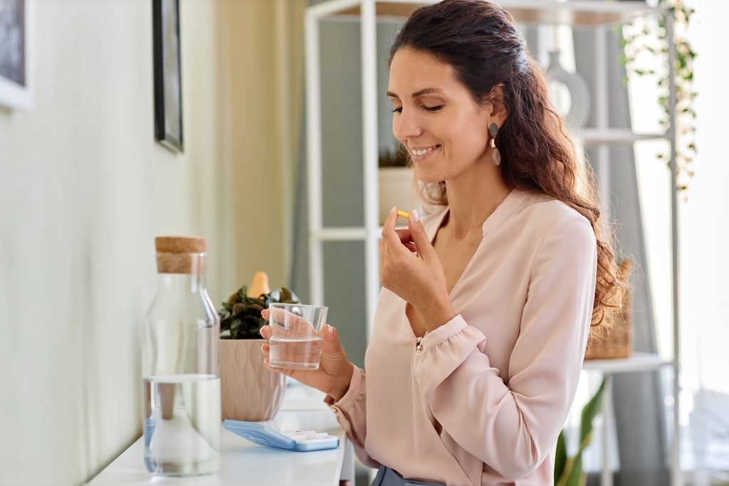 Mulher tomando vitamina c lipossomal com um copo de água na mão