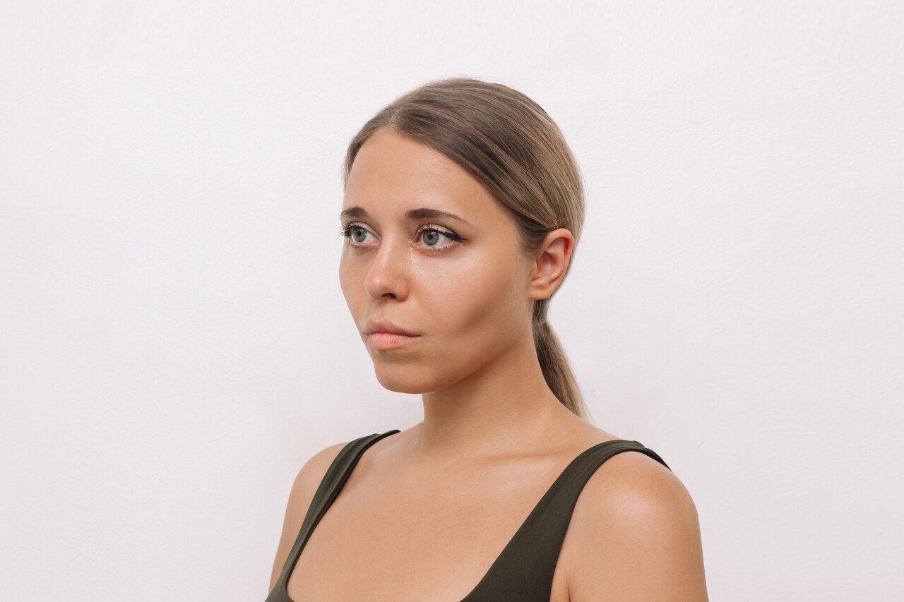 Perfil de uma jovem mulher com cabelo castanho amarrado em um rabo de cavalo, olhando para o lado esquerdo, com bochechas fundas