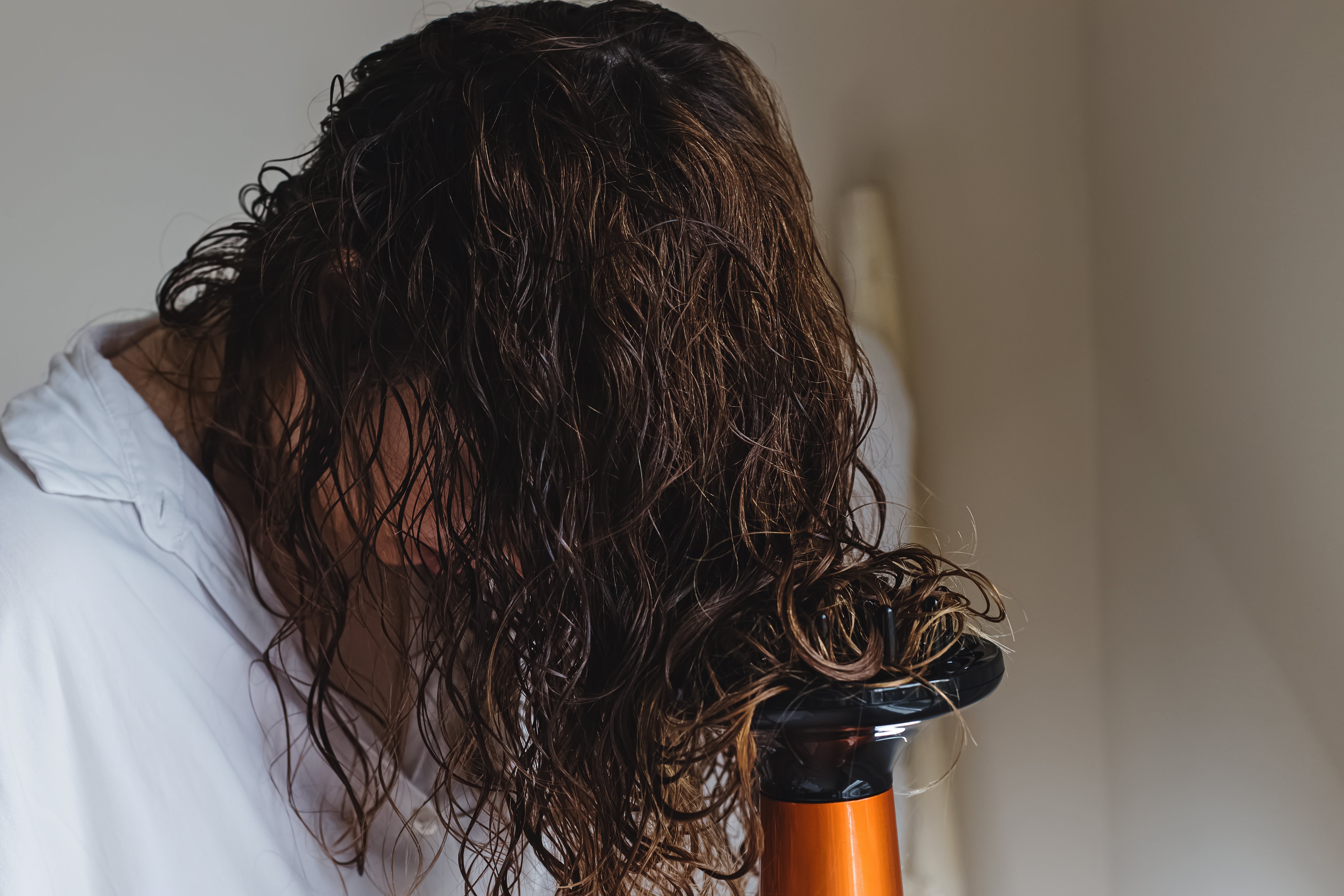 Foto de mulher secando o cabelo cacheado molhado com um difusor acoplado a um secador de cabelo