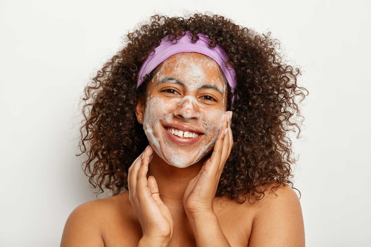 Mulher sorridente aplicando sabonete para pele oleosa no rosto