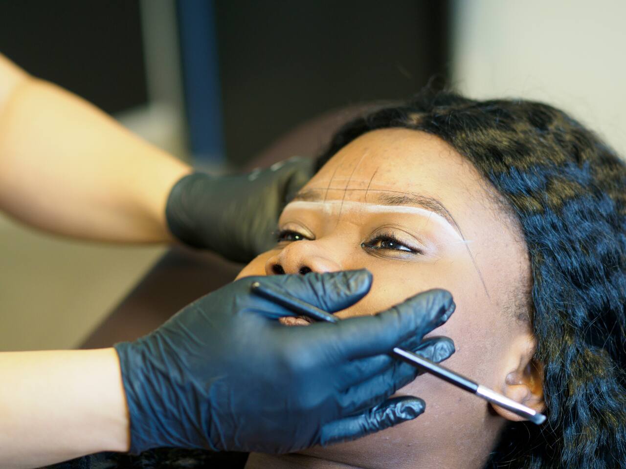Profissional usando luvas pretas fazendo marcação para sobrancelha fio a fio em cliente