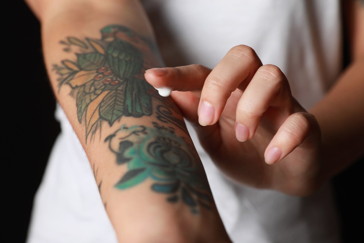 Tatuagens no braço de pessoa aplicando creme