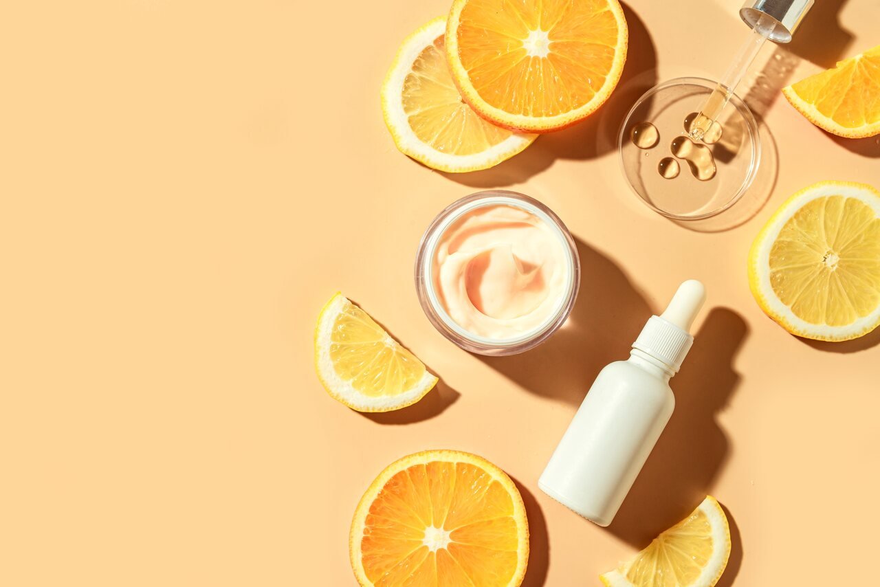 Foto de sérum de vitamina C cercado por fatias de laranja representando ingredientes naturais para cuidados com a pele 