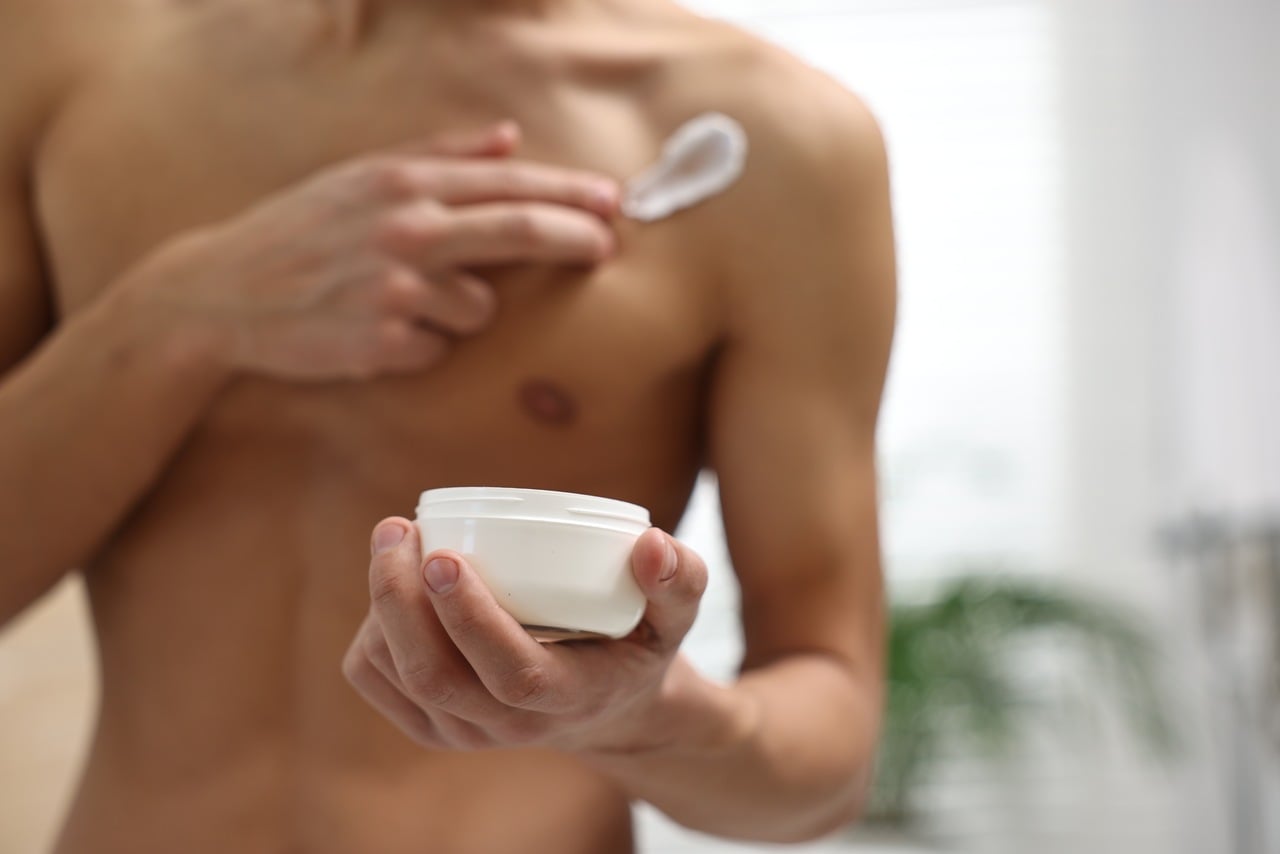 Homem jovem passando creme masculino no corpo