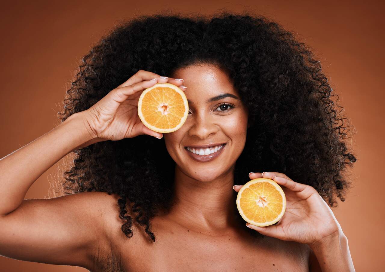 Jovem garota posando com uma laranja fatiada, alimento rico no complexo de vitamina C, em destaque.