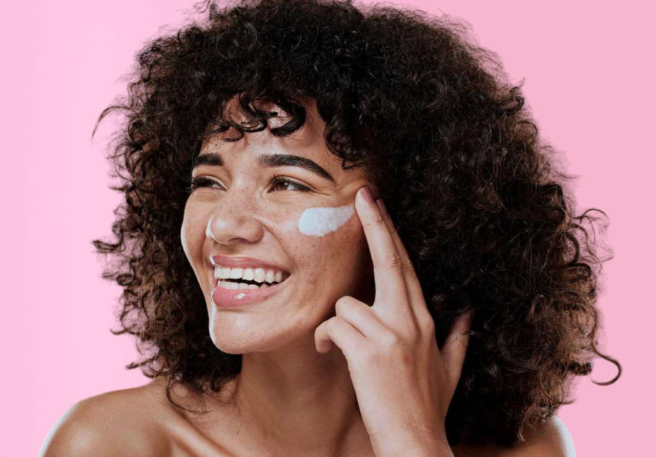 Mulher sorrindo enquanto aplica protetor solar líquido no rosto