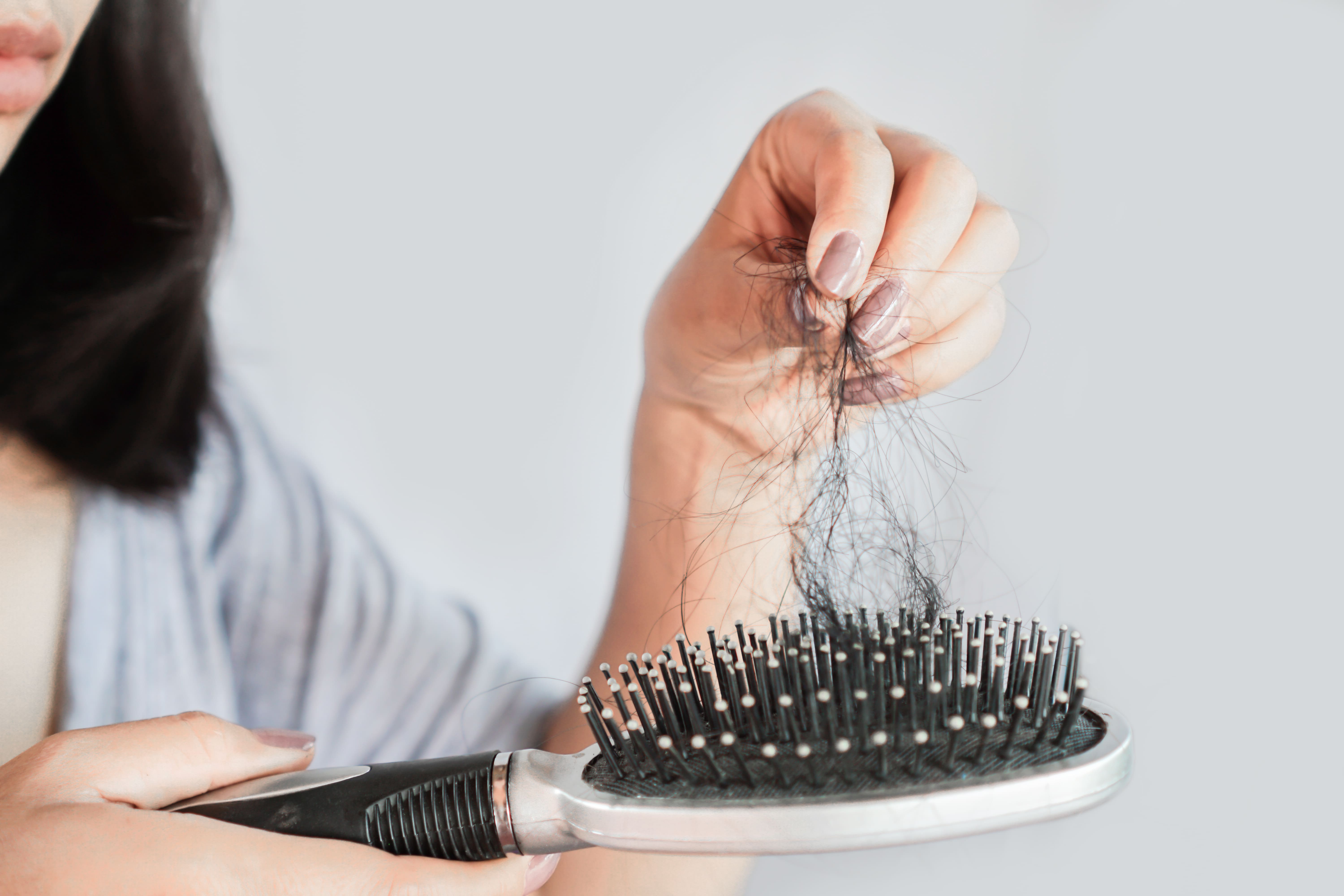 Foto de mulher limpando o pente de cabelo após queda excessiva, queda de cabelo é um dos sintomas de sífilis.